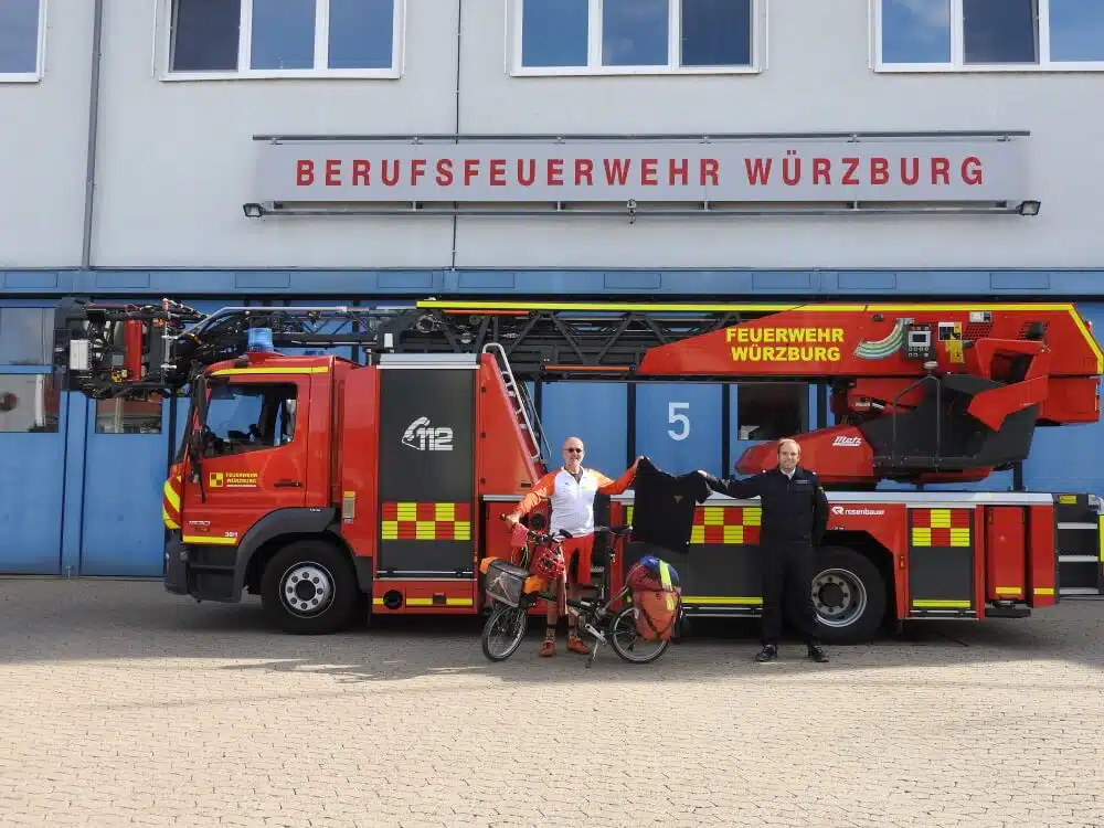 Brandoberinspektor Christoph Hartmann (rechts) überreicht dem ehemaligen Feuerwehrmann Jörg Richter ein Poloshirt, dass ihn an seine Radtour vom Mittelmeer über die Alpen nach München erinnern soll.