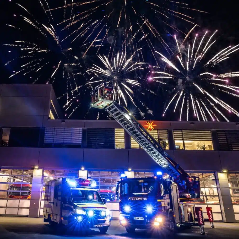 Zwei Feuerwehrautos begrüßen unter einem Feuerwerk das neue Jahr. Doch leider war die Silvesternacht 2021/22 für viele Feuerwehren einsatzreich.
