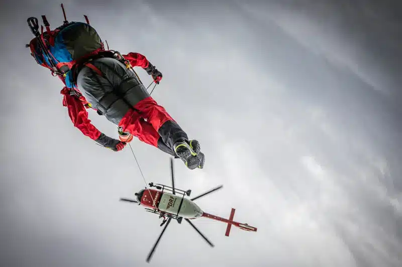 Ein Hubschrauber und ein Retter, an einem Seil hängend, auf luftiger Höhe