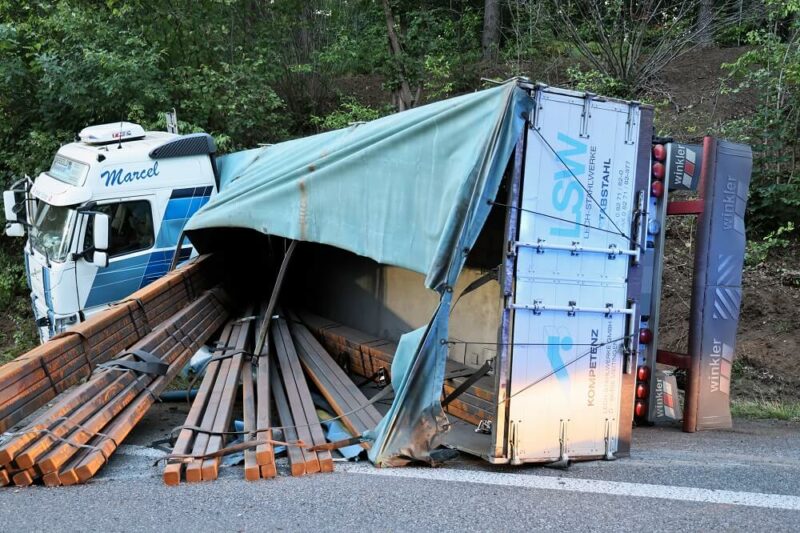 Der Lkw ist umgekippt und diverse Stahlträger liegen auf der Straße.