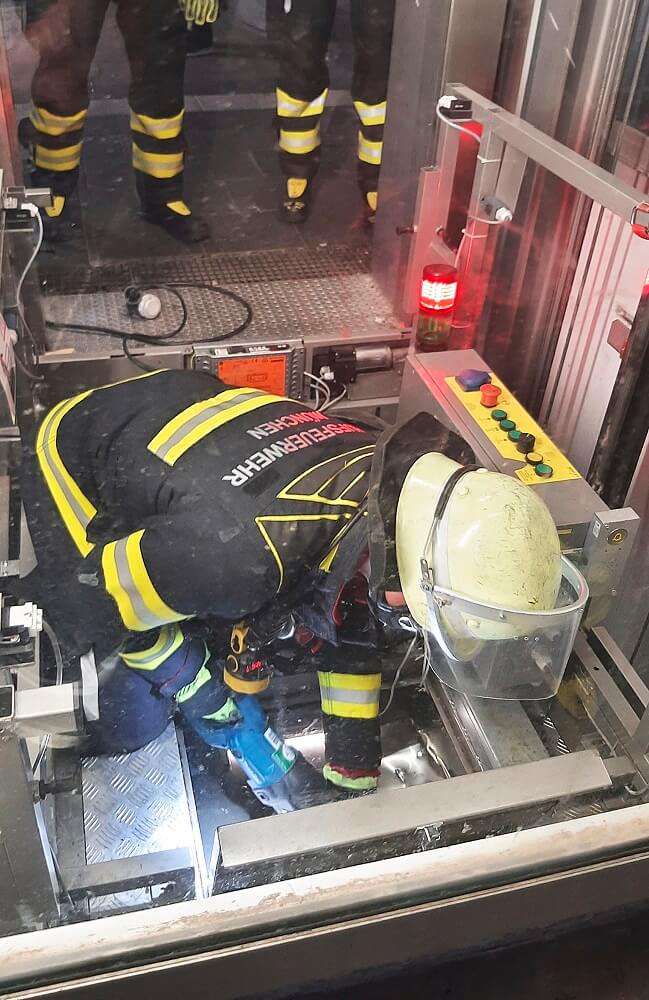 Mit einer Säbelsäge schneidet eine Feuerwehrkraft eine Öffnung in das Aufzugdach.