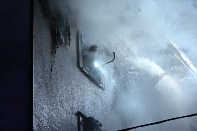 Rauch dringt aus der Wohnung. Ein Feuermann mit einer Taschenlampe leuchtet seine Umgebung aus. 
