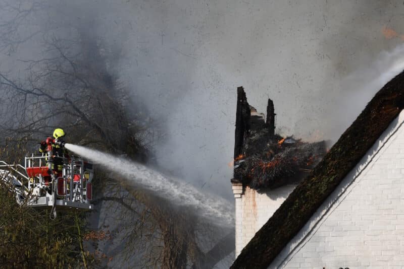 Feuerwehreinsatzkraft löscht das brennende Reetdach.