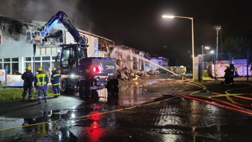 THW-Unterstützung: Nachdem das Feuer durch den Außenangriff unter Kontrolle gebracht wurde, wird die Fassade des Gebäudes mit einem Bagger geöffnet, um an weitere Glutnester heranzukommen. (Foto: Feuerwehr Lennestadt)